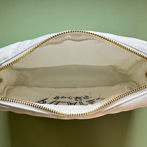 May include: White canvas zippered pouch with a gold zipper. The pouch has the words "Be Brave" printed on the inside.