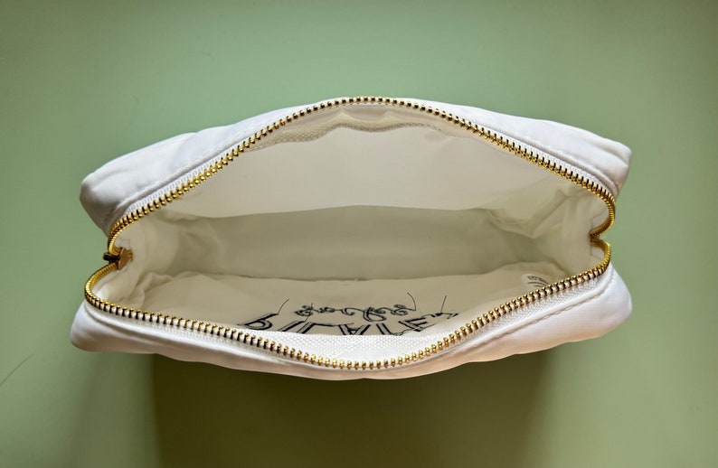 May include: White canvas zippered pouch with a gold zipper. The pouch has the words "Be Brave" printed on the inside.