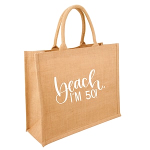 Könnte beinhalten: Eine braune Jute-Tragetasche mit weißem Text, der "Beach. I'm 50!" lautet.
