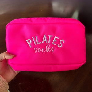 May include: A bright pink pouch with the words "PILATES socks" embroidered in white.