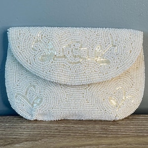 May include: A white beaded clutch purse with a floral design. The purse is made of small, white beads and has a flap closure.