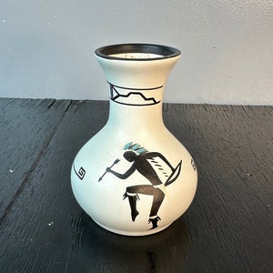 May include: White ceramic vase with a black rim and a black and white design of a Native American dancer with a blue headdress.