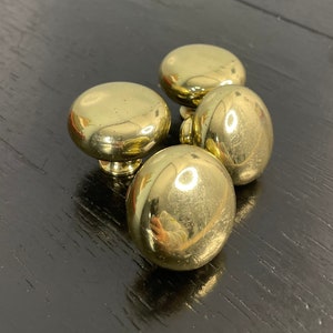 May include: Four gold-toned round cabinet knobs with a smooth, shiny finish.