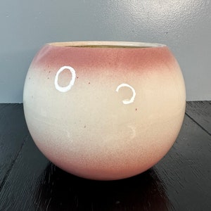 May include: A large, round, white planter with a pink ombre glaze. The planter is made of ceramic and has a smooth, glossy finish.