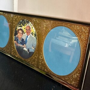 May include: A gold-toned picture frame with three oval openings. The center opening features a photo of an older couple. The other two openings are empty.
