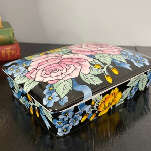 May include: A black rectangular trinket box with a floral design. The box is decorated with pink, yellow, blue, and green flowers on a black background.