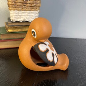 May include: A terracotta bird figurine with a black and white geometric design on its wing. The bird is sitting on a black surface.