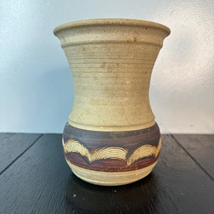May include: A small, beige ceramic vase with a brown and white geometric pattern around the middle.