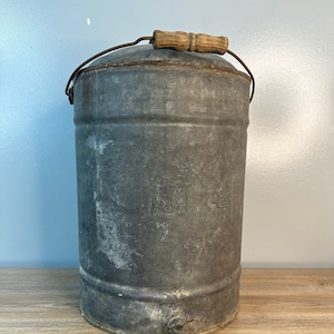 Puede incluir: Un enfriador de agua vintage de metal galvanizado con un asa de madera y un grifo. El enfriador tiene un aspecto rústico y desgastado y es perfecto para agregar un toque de encanto rústico a tu hogar.
