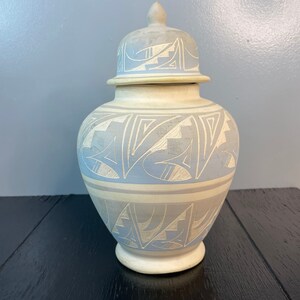 May include: A white ceramic jar with a lid, decorated with a blue and white geometric pattern. The jar has a rounded body and a wide mouth.