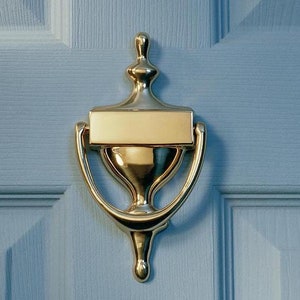 May include: A gold door knocker with a rectangular nameplate on a light blue door.