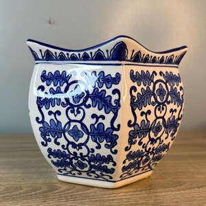 Puede incluir: Una maceta de cer&aacute;mica blanca con un estampado floral azul. La maceta tiene un borde festoneado y una forma geom&eacute;trica. El dise&ntilde;o azul presenta hojas y motivos florales. Adecuado para uso en interiores o exteriores.