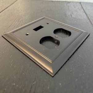 May include: Black electrical outlet cover plate with a single light switch and two outlets.