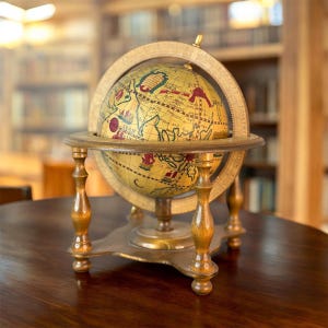 May include: A vintage-style globe with a detailed map design, mounted on a wooden stand. The globe features a cream-colored surface with red and green accents, and is encased in a wooden meridian ring. The stand has a dark brown finish.