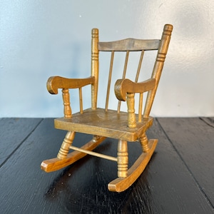 May include: A small wooden rocking chair with a natural wood finish. The chair has a simple design with a curved back and arms.
