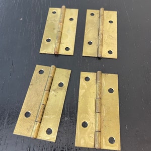 May include: Four brass hinges with a brushed finish. The hinges are rectangular and have a series of holes along the edges.