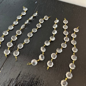 May include: Seven strands of clear crystal beads strung on gold wire. Each strand has a hook at the top.