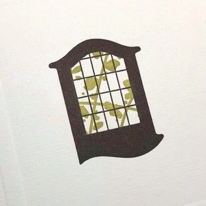 May include: A white card with a brown and green window design. The window has a grid pattern and a floral design inside.