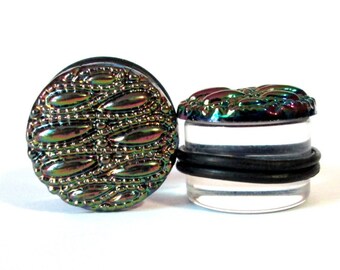 May include: A pair of iridescent black ear gauges with a clear acrylic backing. The front of the gauges features a textured, patterned design.