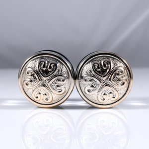 Peut inclure: Une paire de jauges d'oreille en argent et or avec un motif de trèfle à quatre feuilles.