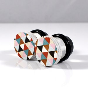May include: Pair of white acrylic ear gauges with a geometric pattern of red, orange, pink, blue, and black triangles.