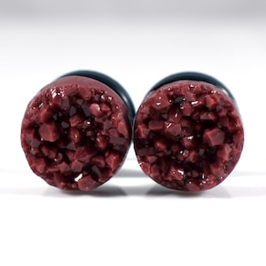 Puede incluir: Un par de expansores de oreja de cristal rojo oscuro con respaldo negro.