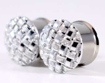 May include: A pair of silver ear gauges with a textured, woven design. The gauges are made of metal and have a shiny finish.