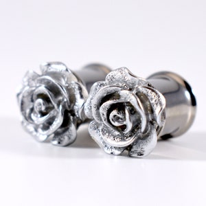 May include: A pair of silver rose-shaped ear gauges. The gauges are made of stainless steel and feature a detailed rose design.