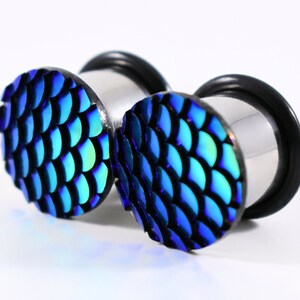 May include: A pair of blue and green iridescent ear gauges with a scale pattern. The gauges are made of stainless steel and have a black o-ring.