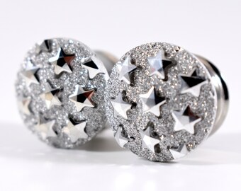 May include: A pair of silver-toned ear gauges with a glittery finish and a star pattern.