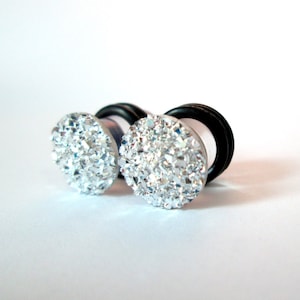 May include: A pair of silver sparkly ear gauges with black rubber backing.