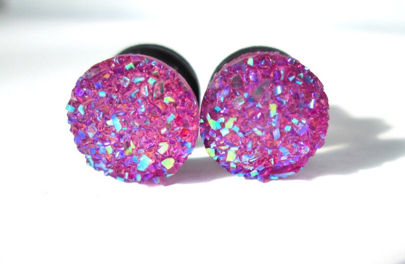 May include: A pair of pink iridescent ear gauges with a glittery finish.