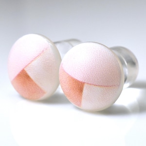 May include: A pair of cufflinks with a clear, rounded post and a circular face. The face of each cufflink is white with a geometric design in pink and peach tones. The cufflinks are set against a white background.