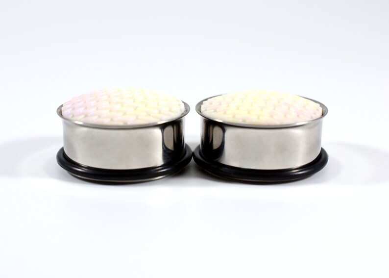 May include: A pair of stainless steel ear gauges with a white and pink patterned design. The gauges are 0g in size.