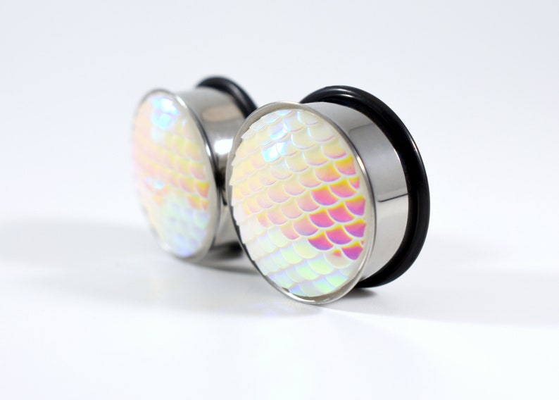 May include: A pair of iridescent white ear gauges with a mermaid scale design. The gauges are made of stainless steel and have a black o-ring.