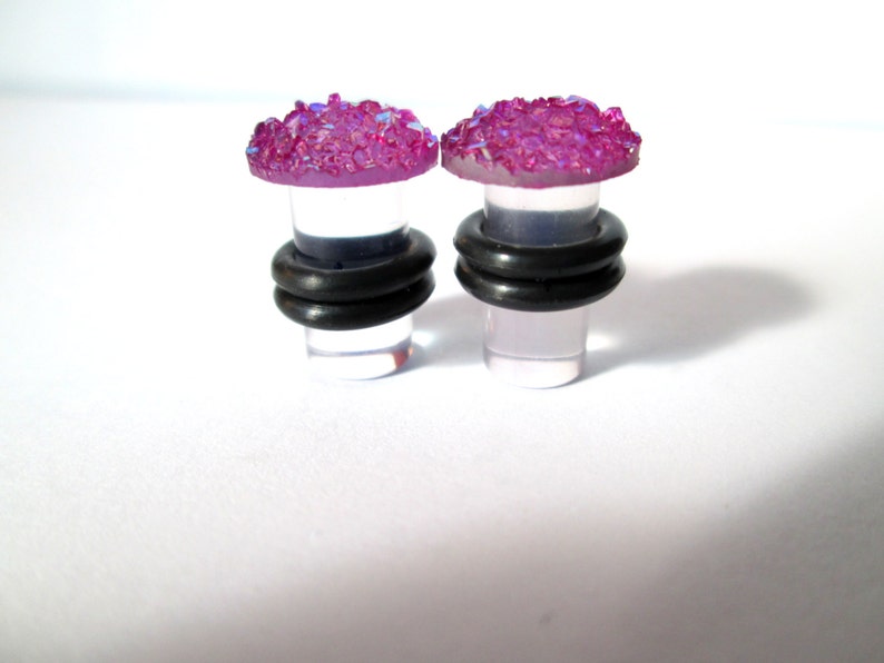 May include: Pair of clear acrylic ear gauges with a pink glitter top. The gauges have a black rubber o-ring around the base.