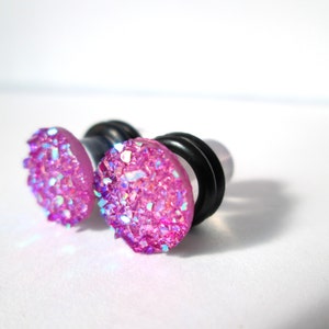 May include: A pair of pink glitter ear gauges with black o-rings. The gauges are made of acrylic and have a sparkly finish.