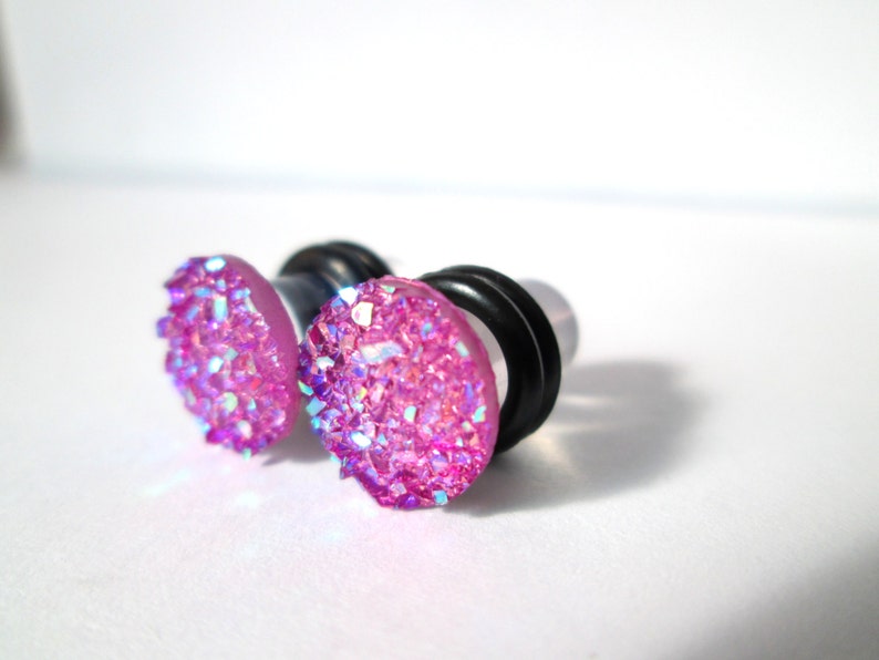May include: A pair of pink glitter ear gauges with black o-rings. The gauges are made of acrylic and have a sparkly finish.