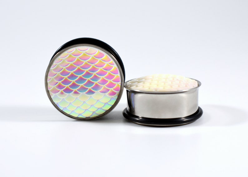May include: A pair of iridescent mermaid scale ear gauges. The gauges are made of stainless steel and have a black o-ring. The scales are a rainbow of colors, including pink, blue, green, and yellow.