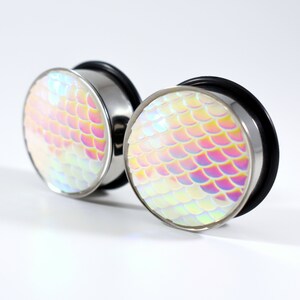 May include: A pair of iridescent silver ear gauges with a mermaid scale design. The gauges are round and have a smooth, polished finish.