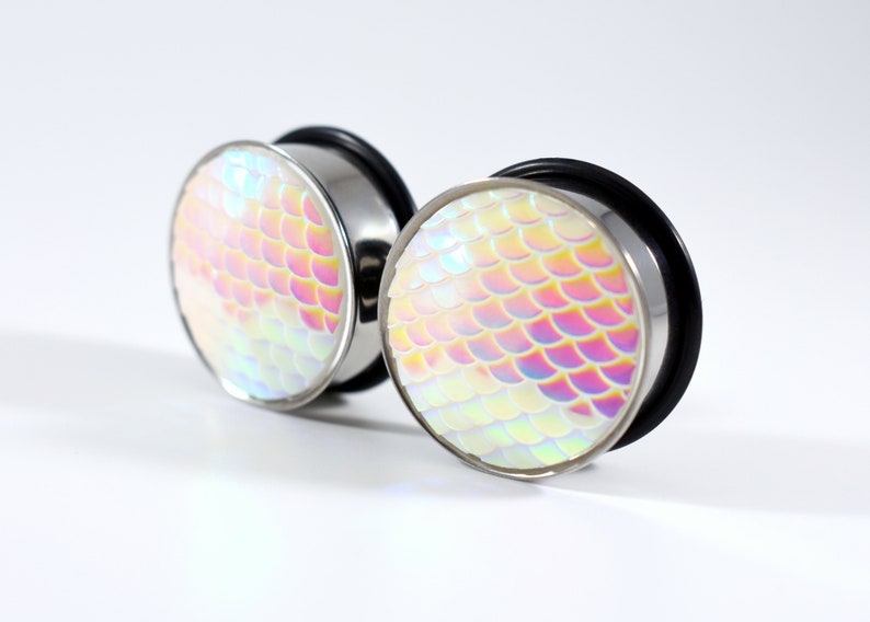 May include: A pair of iridescent silver ear gauges with a mermaid scale design. The gauges are round and have a smooth, polished finish.