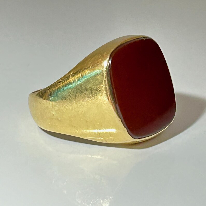 May include: A gold ring with a red carnelian stone. The ring has a simple, classic design.
