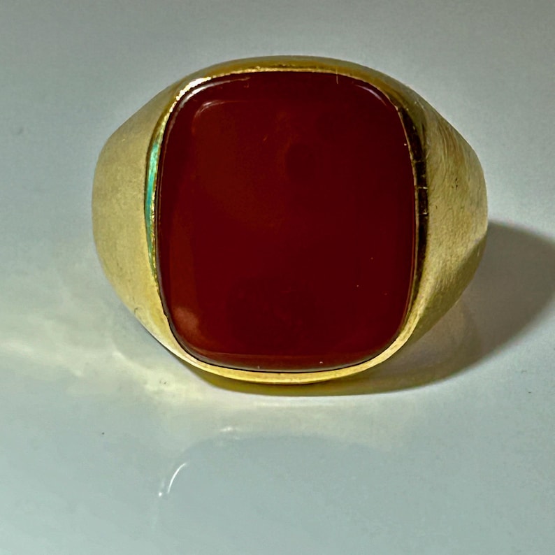 May include: A gold ring with a large, square, red carnelian gemstone.