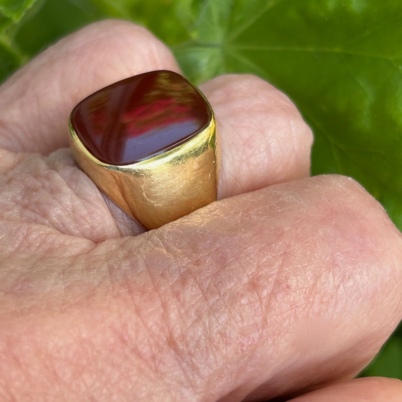May include: A gold ring with a square, red carnelian gemstone.