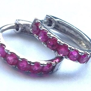 May include: A pair of silver hoop earrings with a row of pink gemstones around the edge.