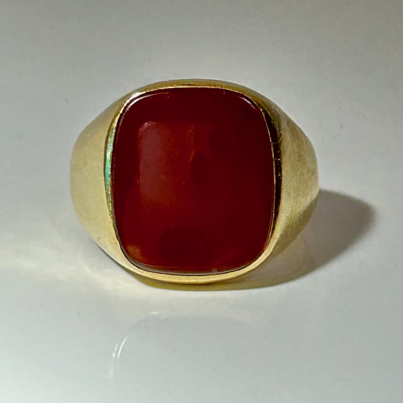 May include: A gold ring with a large, red carnelian gemstone.