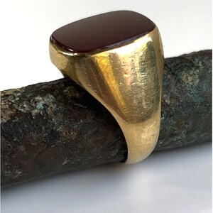May include: A gold signet ring with a dark red rectangular gemstone.