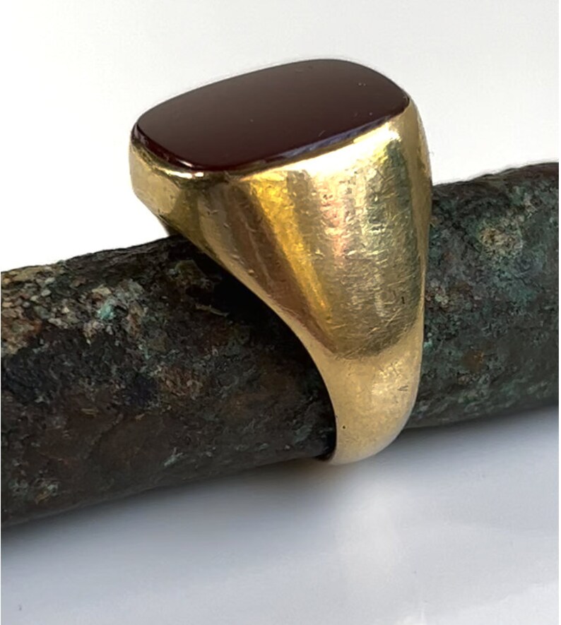 May include: A gold signet ring with a dark red rectangular gemstone.