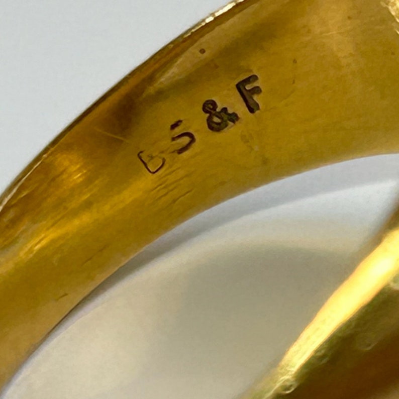 May include: Close-up of the inside of a gold ring with the inscription "S & F" on the band.