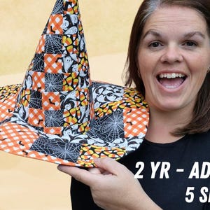 Könnte beinhalten: Ein Patchwork-Hexenhut für Halloween mit breiter Krempe. Der Hut hat ein sich wiederholendes Muster aus orangefarbenen und weißen karierten Quadraten, Spinnweben, Geistern und Zuckermais. Der Text auf dem Bild lautet "2 YR - ADULT 5 SIZES".
